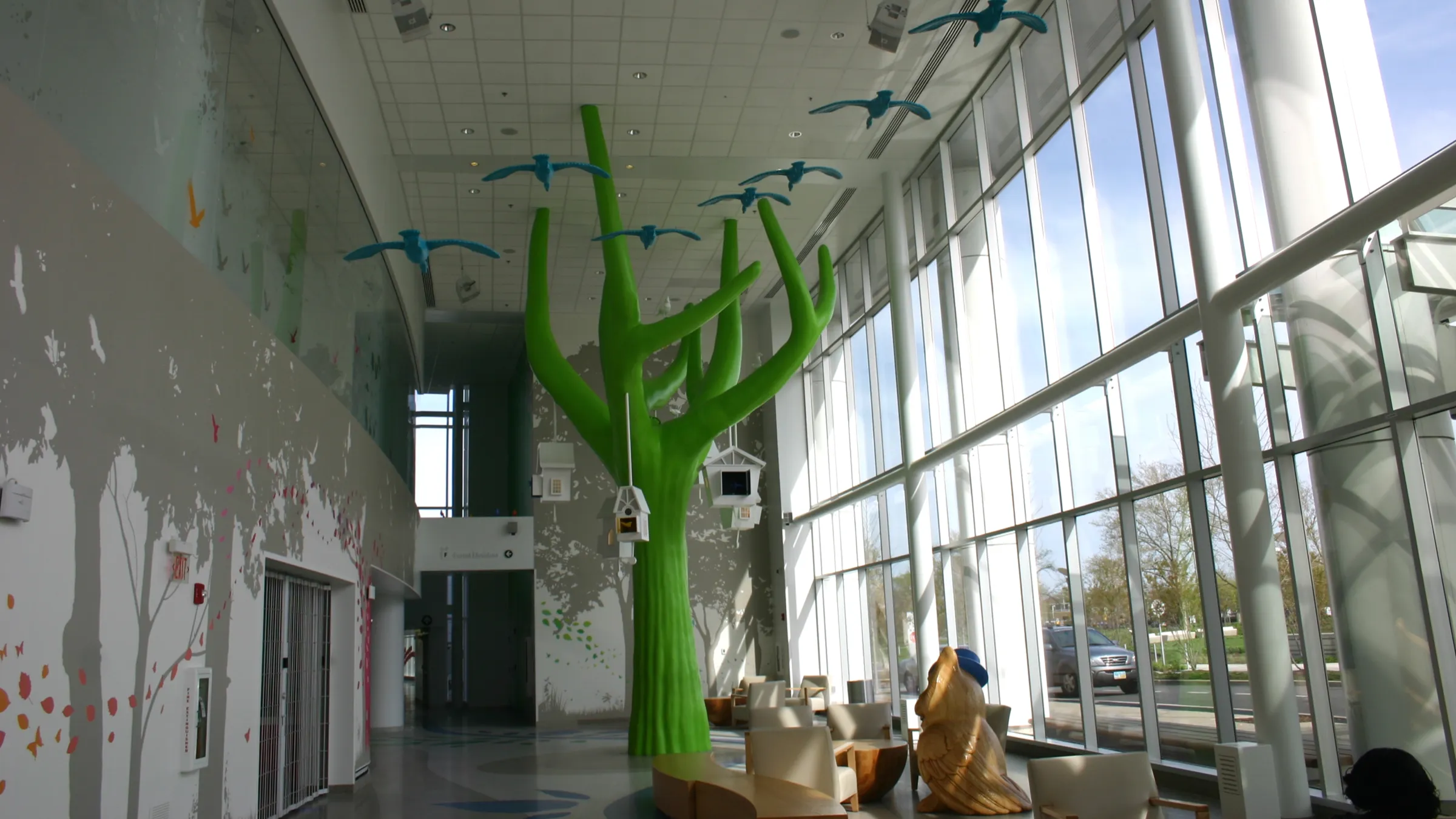 Tree in hospital hallway with birds flying and hanging birdhouses